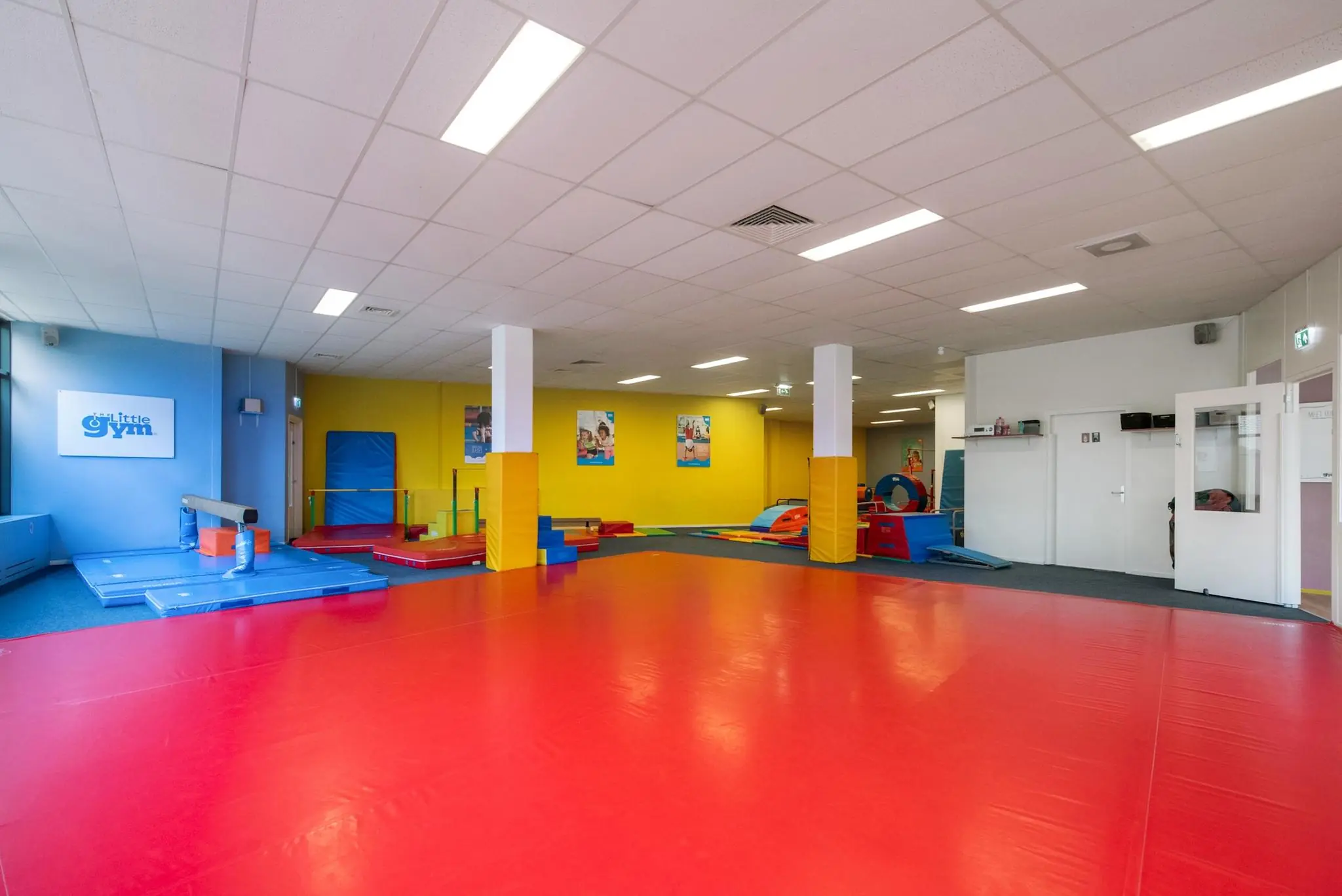 Kleurrijke binnenspeelruimte van The Little Gym aan de Koningin Julianalaan met zachte gymtoestellen en een rode matvloer.
